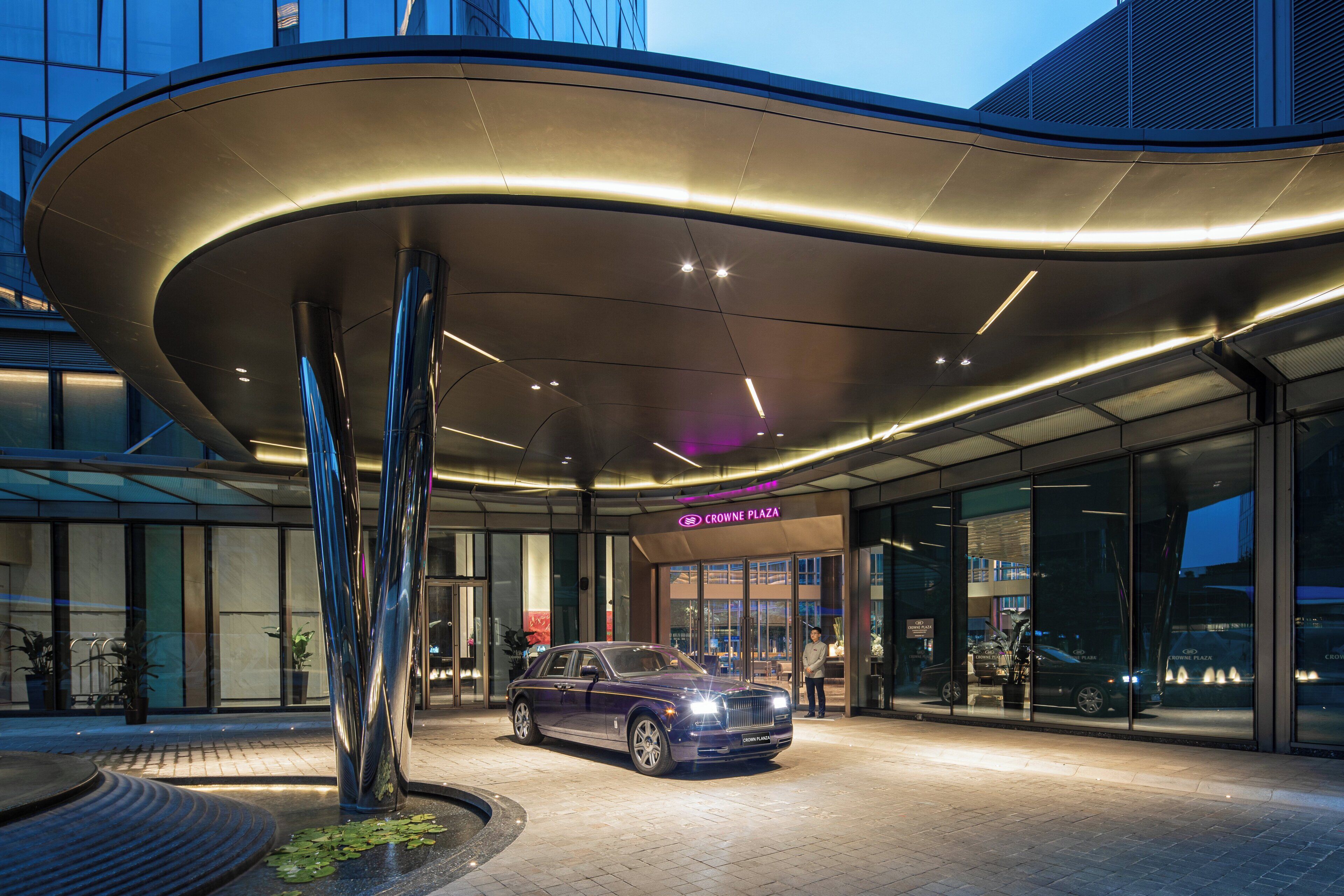 A modern building entrance with a Rolls Royce parked in front.