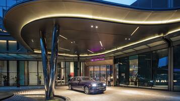 A modern building entrance with a Rolls Royce parked in front.