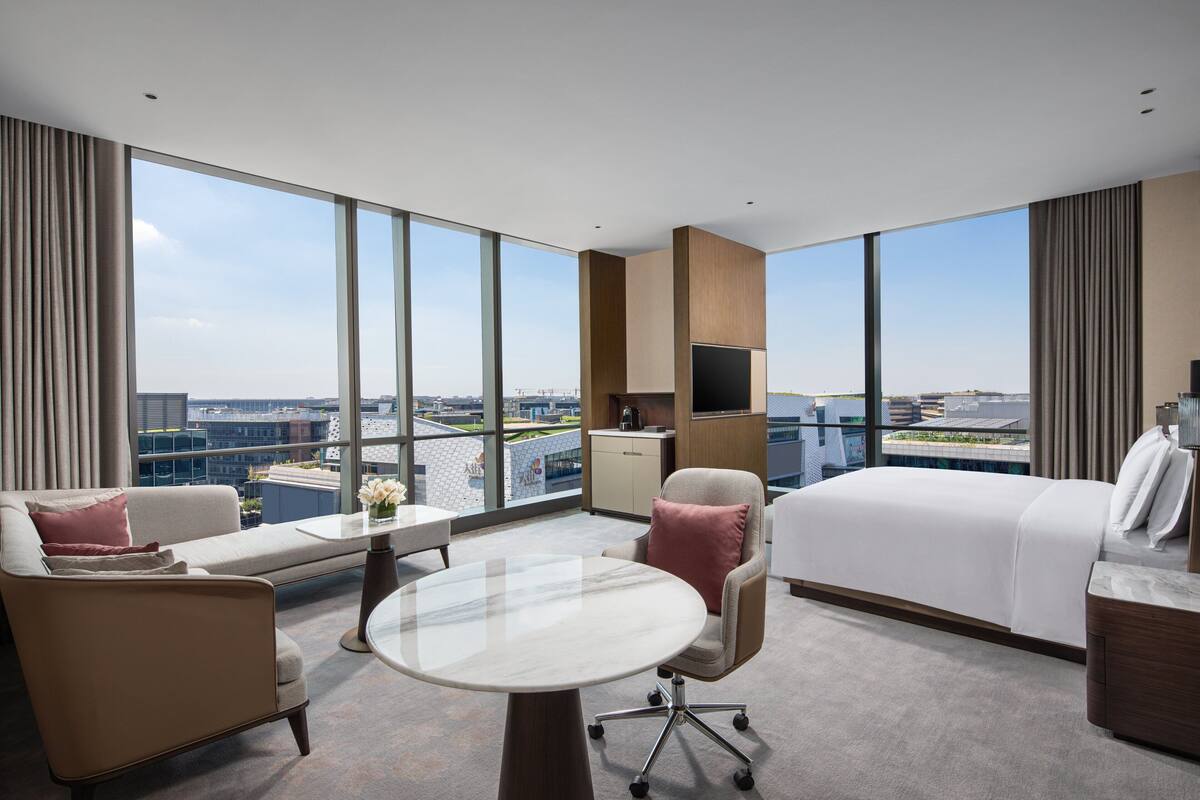 Ein modernes Hotelzimmer mit einem großen Bett, einer Sitzecke, einem Schreibtisch und Blick auf die Stadt.