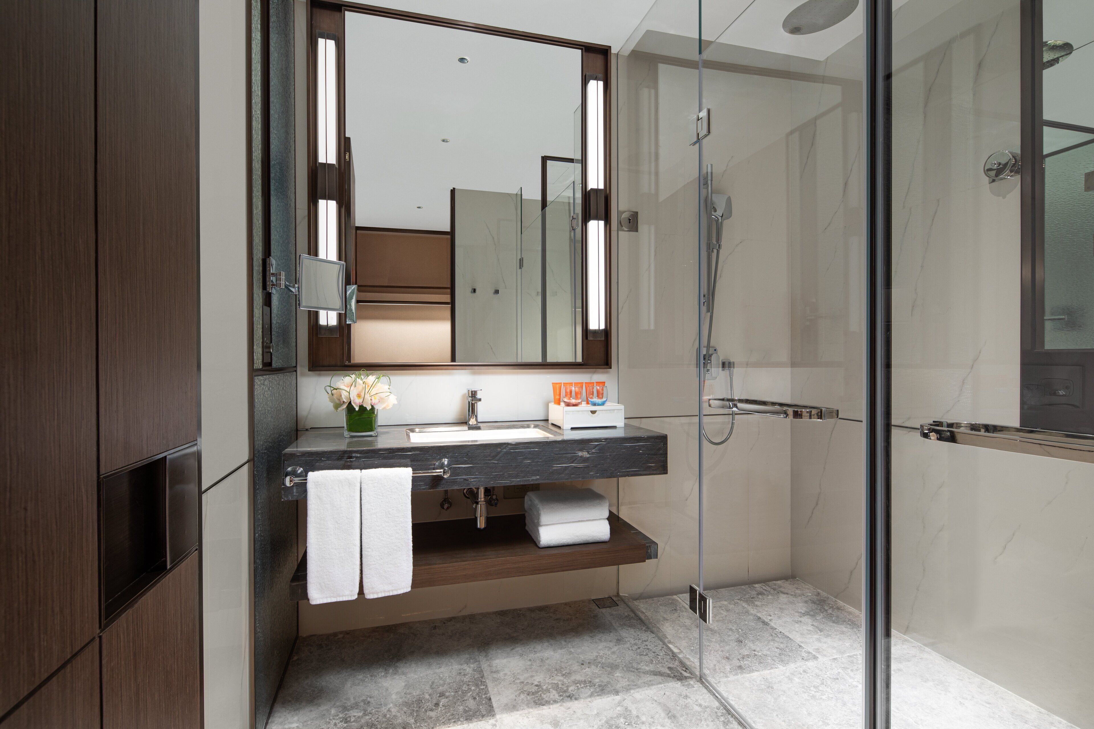 A modern bathroom with a glass shower enclosure, a marble countertop sink, and a wooden vanity.