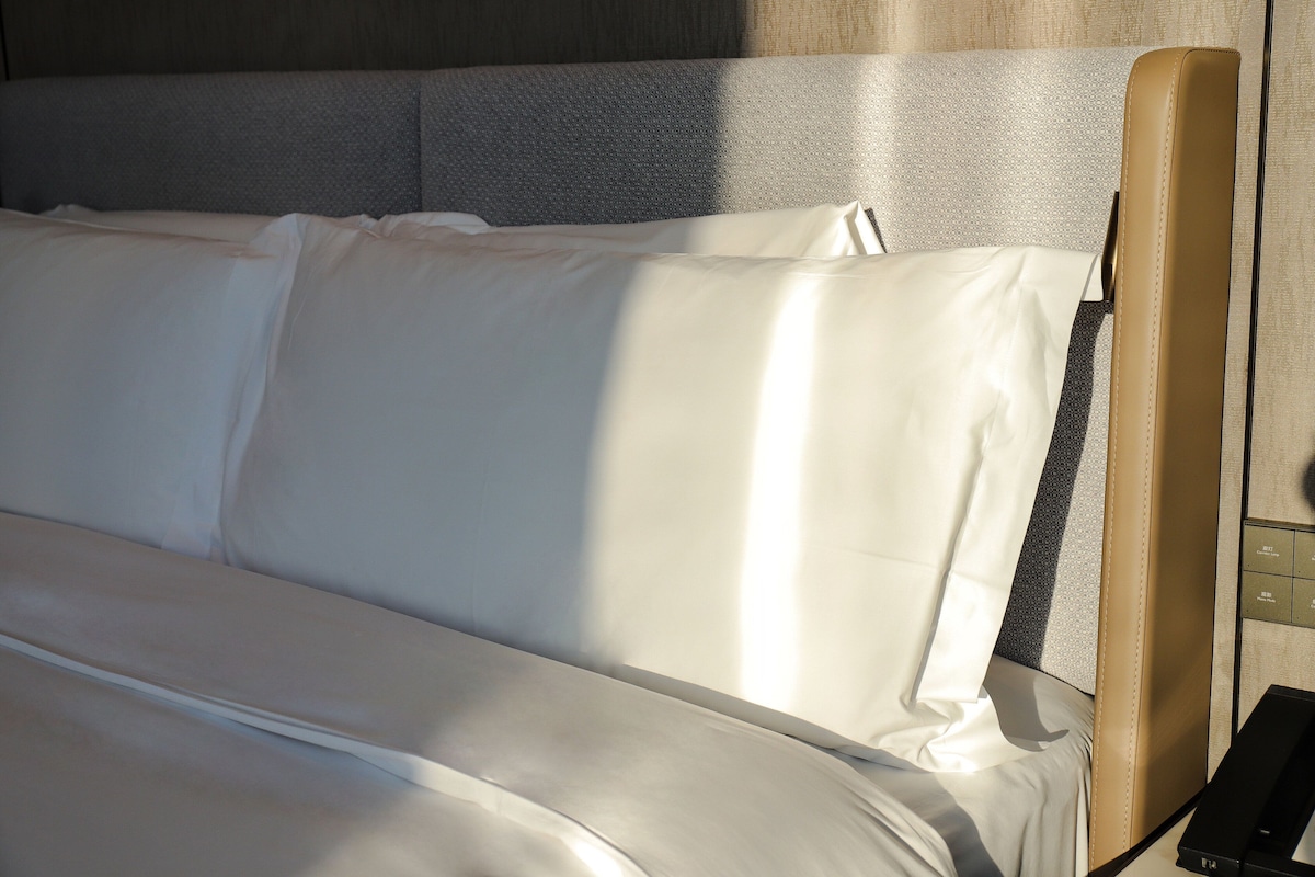 Una cama con sábanas blancas y cabecera con panel gris texturizado.
