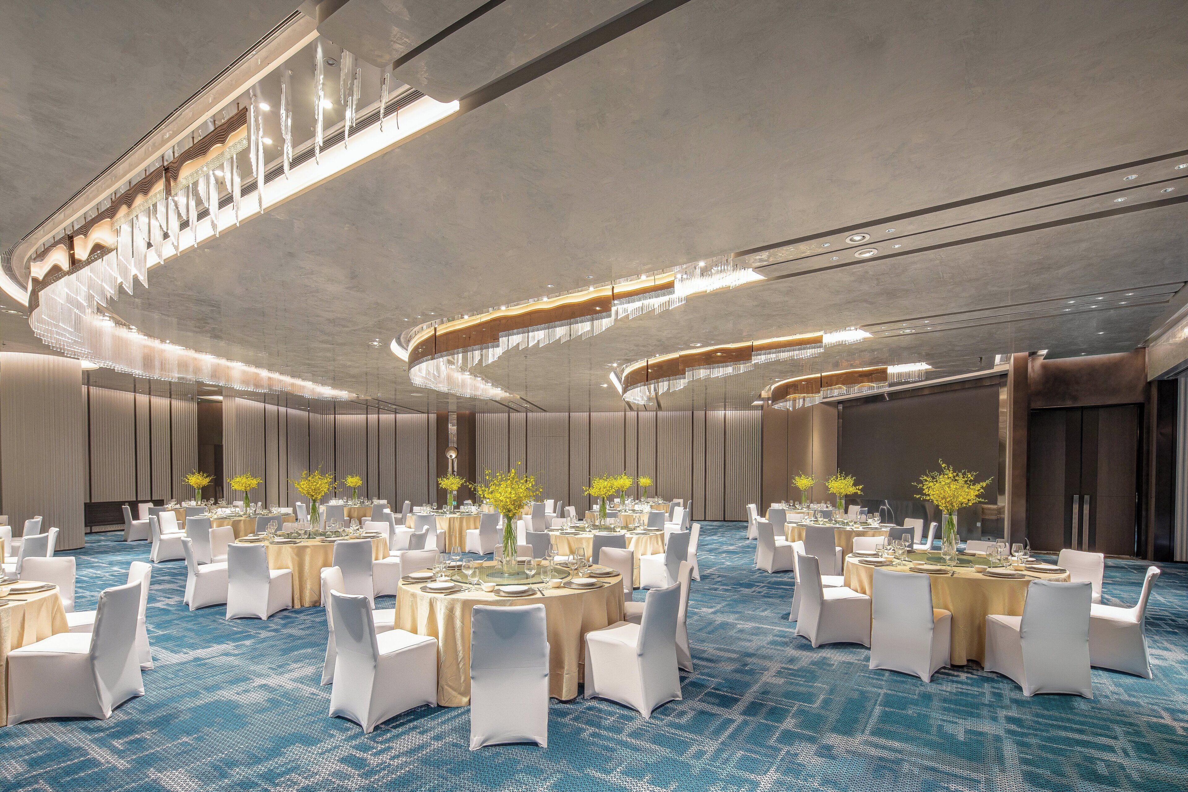 A banquet hall with round tables, white chairs, and floral centerpieces.