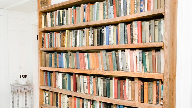 A large wooden bookshelf filled with books in a room with wooden flooring and white walls. - Historic 1880 Farmhouse with Modern Southern Charm (Casar)