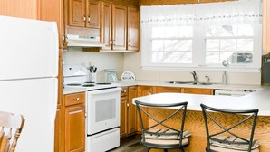 A kitchen with wooden cabinets, a white refrigerator, a stove, and two bar stools. - Historic 1880 Farmhouse with Modern Southern Charm (Casar)