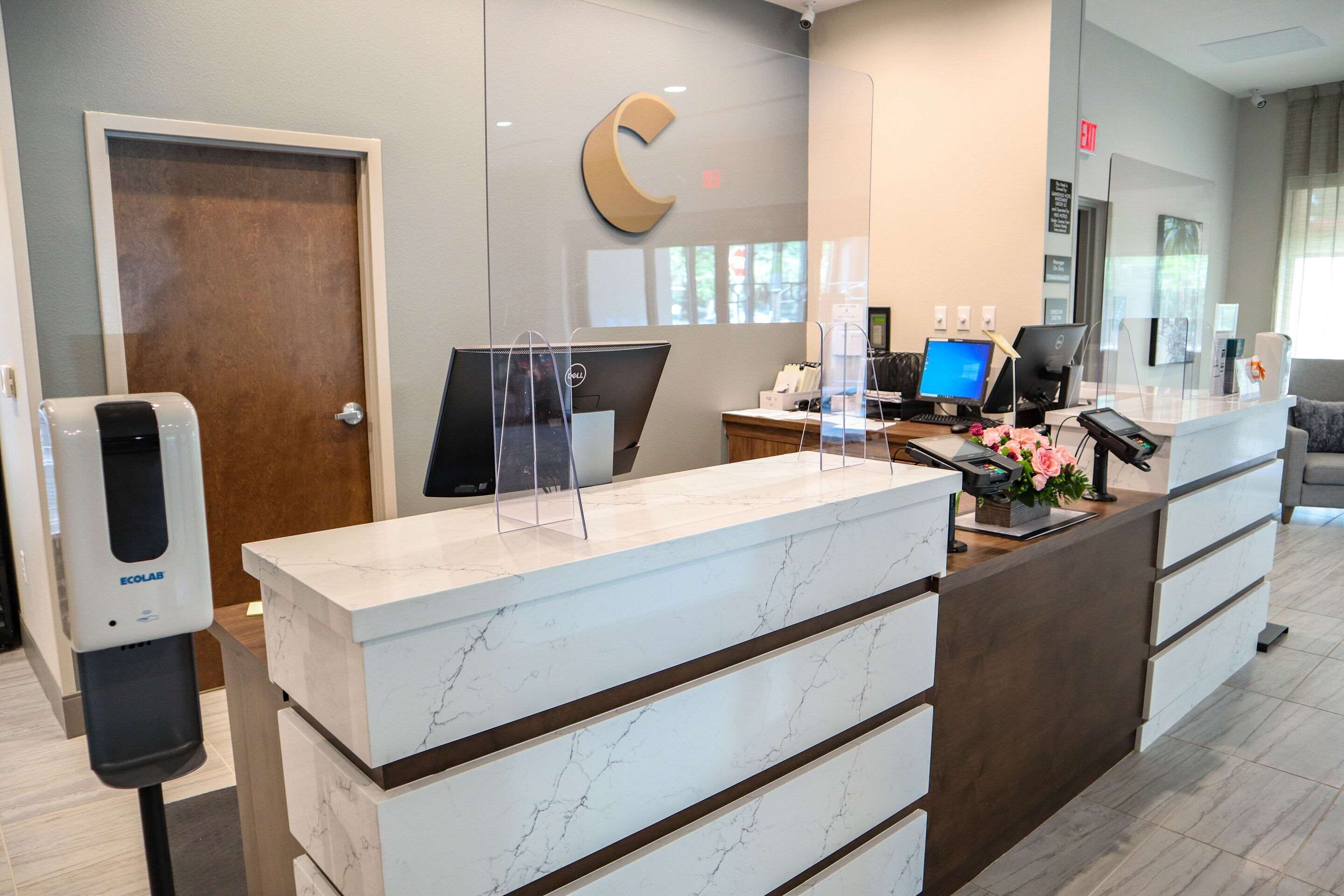 A reception desk with a marble top, a wooden door, and a large C logo on the wall.