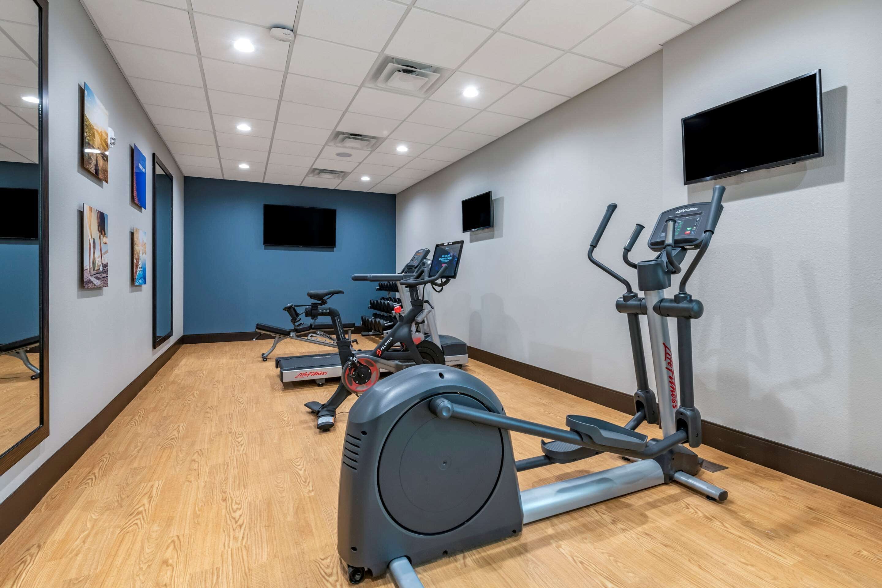 Un gimnasio con equipo cardiovascular, un televisor y obras de arte en las paredes.