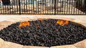 A fire pit area surrounded by stone tiles, with a metal fence in the background.