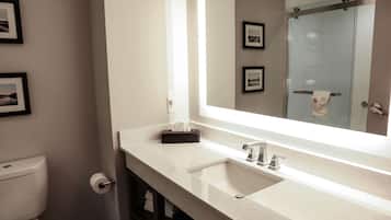 Une salle de bain moderne avec un lavabo blanc, un grand miroir et une porte de douche en verre.