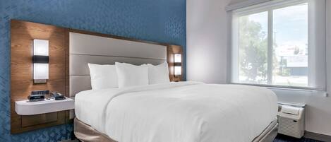 Een hotelkamer met een groot bed, een nachtkastje met een wekker en een raam met uitzicht op de omgeving.