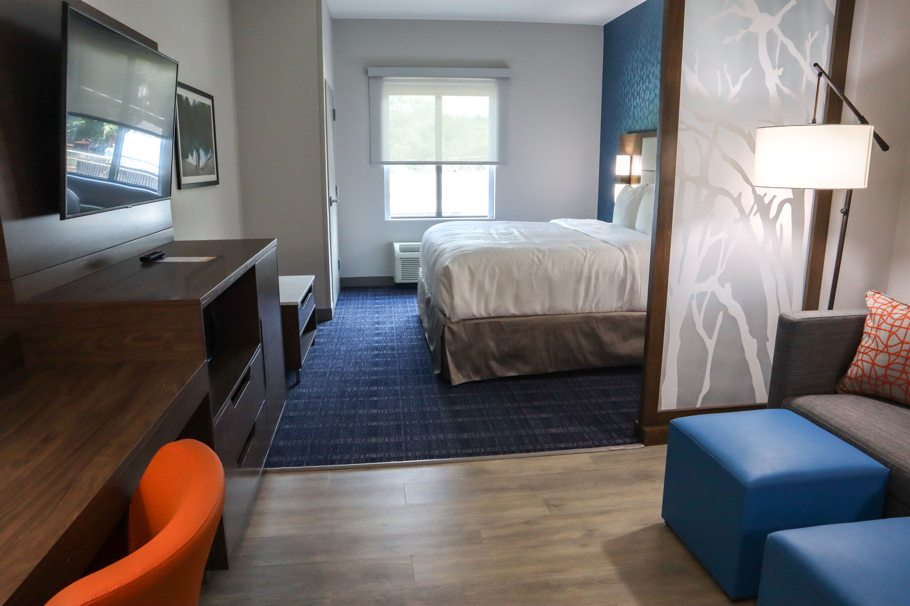 Habitación de hotel con cama, escritorio, silla, televisión, ventana y lámpara.