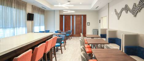 A modern dining area with long tables and chairs, a wooden door, and a wall-mounted TV.