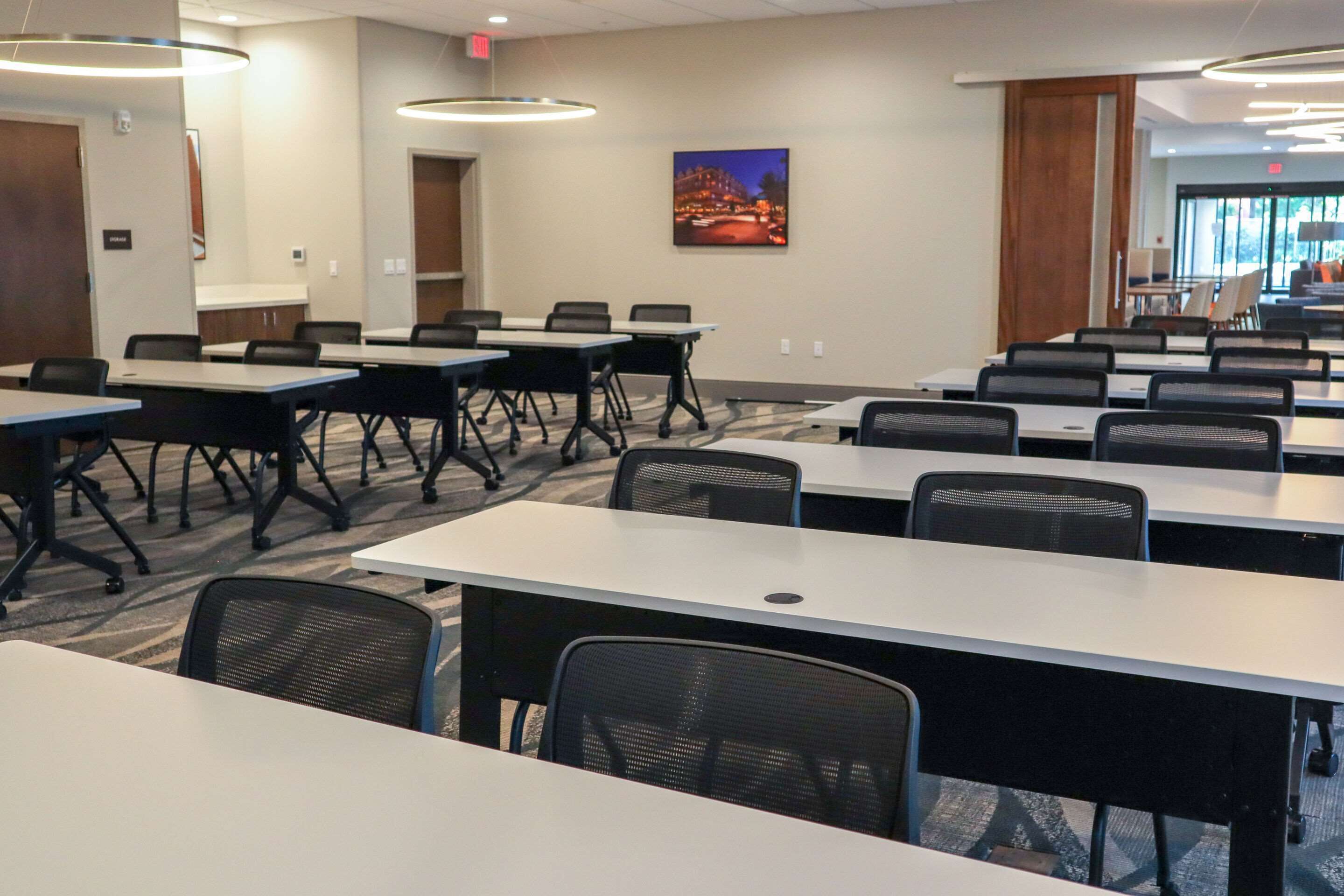 Une salle de conférence dotée de plusieurs tables et chaises, d’un grand tableau accroché au mur et offrant une vue sur l’espace extérieur grâce aux portes vitrées.