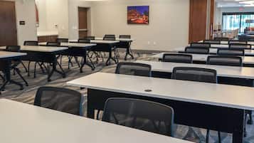Une salle de conférence dotée de plusieurs tables et chaises, d’un grand tableau accroché au mur et offrant une vue sur l’espace extérieur grâce aux portes vitrées.