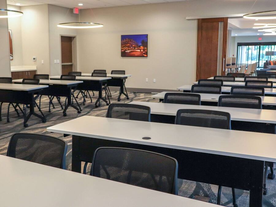 Une salle de conférence dotée de plusieurs tables et chaises, d’un grand tableau accroché au mur et offrant une vue sur l’espace extérieur grâce aux portes vitrées.
