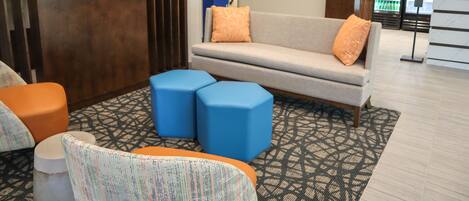 Un hall d’entrée avec un canapé, deux poufs bleus et un fauteuil à motifs.