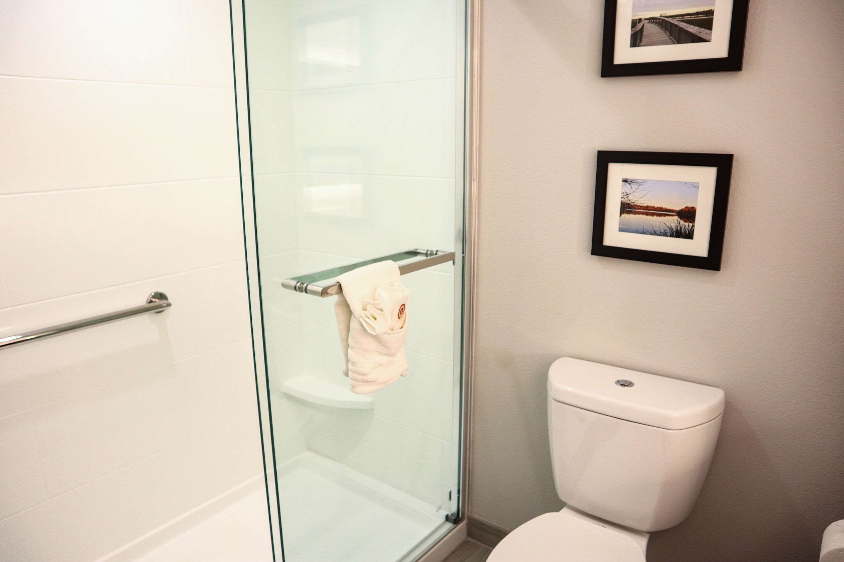 Un baño con cabina de ducha de vidrio, inodoro blanco y dos cuadros en la pared.