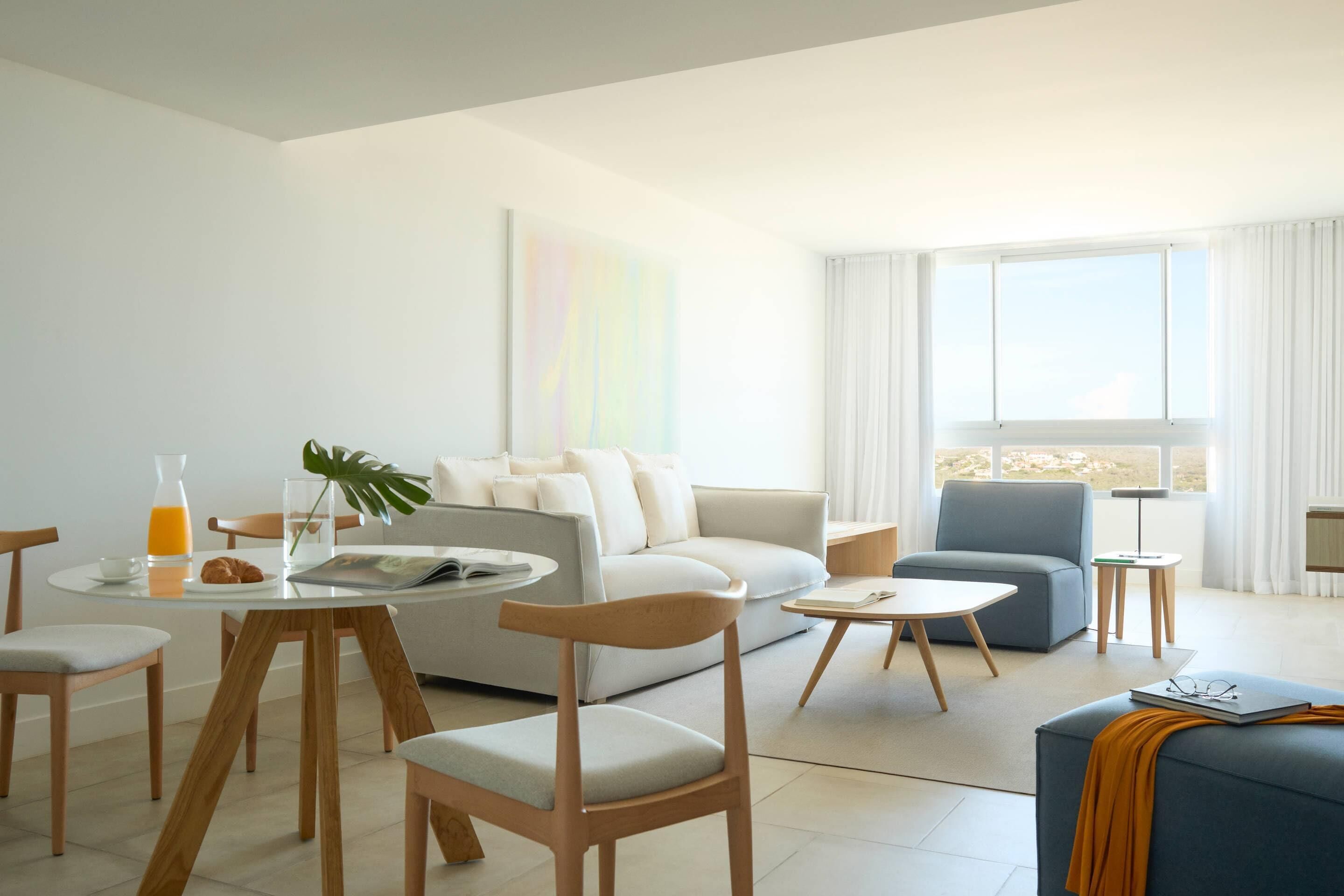 A modern living room with a sofa, two armchairs, a coffee table, and a dining table with chairs.