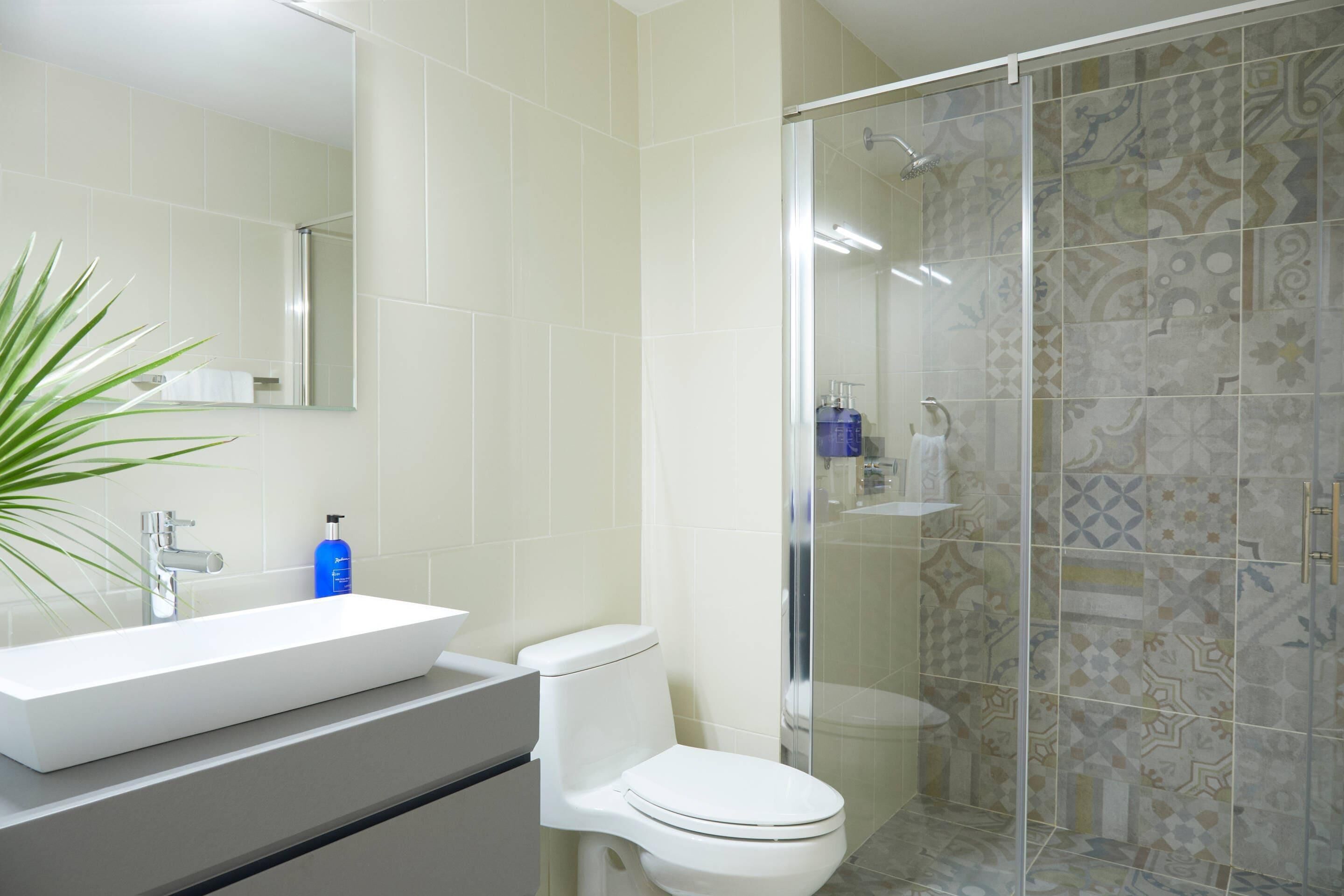 A bathroom with a white sink, a toilet, and a shower area with patterned tiles.