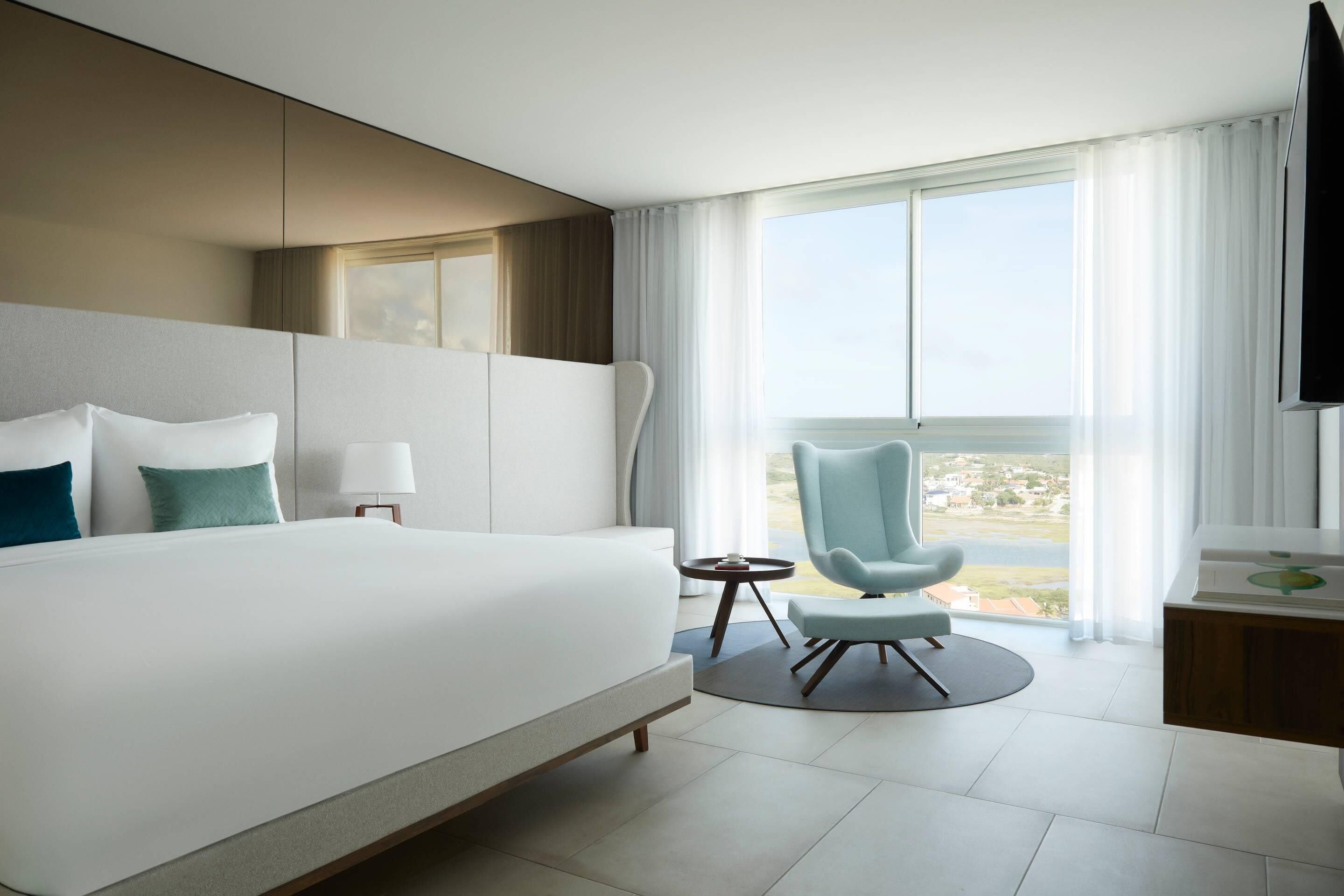 Habitación de hotel moderna con una cama grande, un escritorio, una silla y vistas a la ciudad.