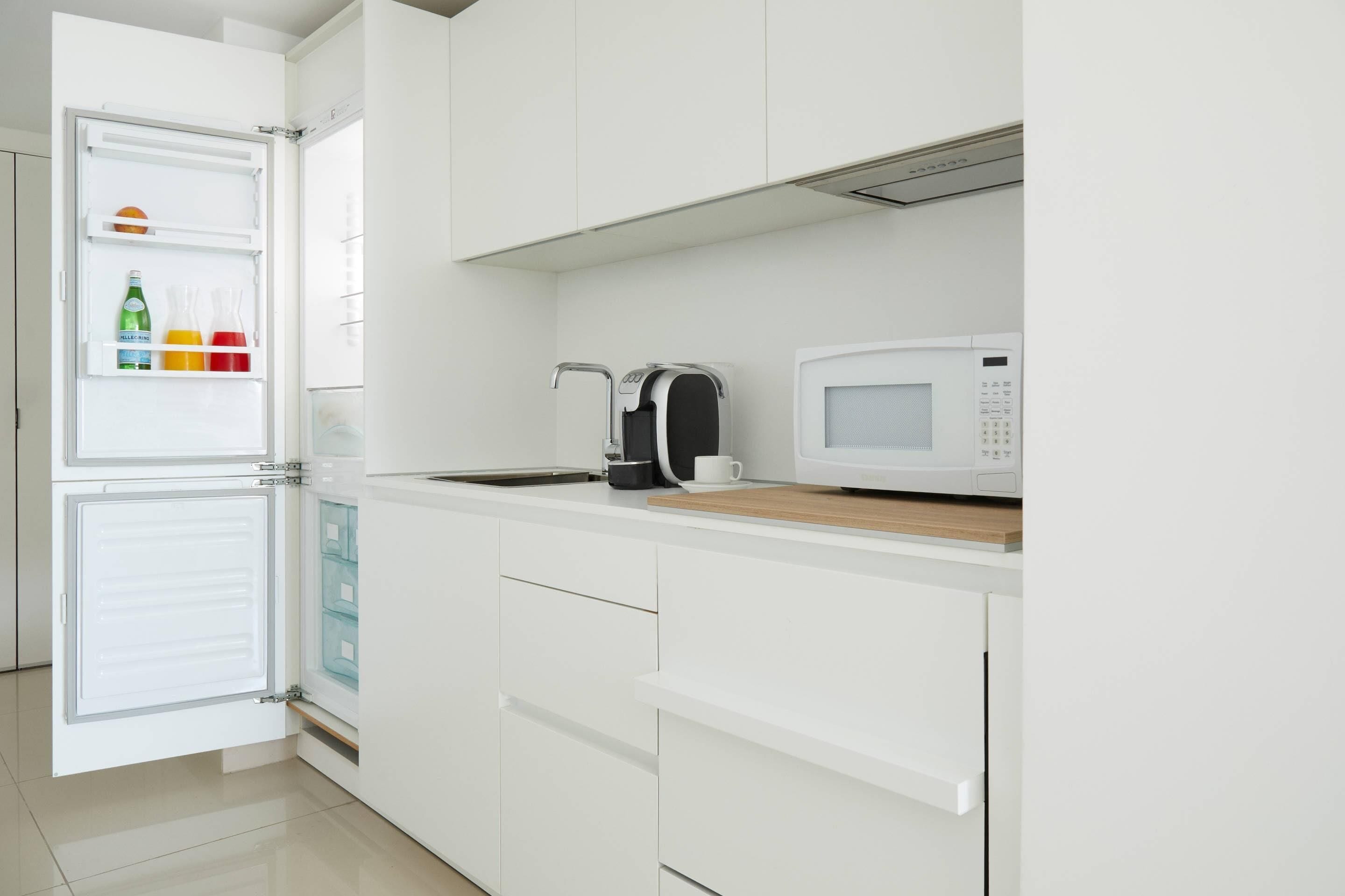 A modern kitchen with a built-in microwave, a coffee machine, and a refrigerator with colorful items inside.