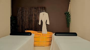 A spa room with a wooden tub, a white robe, and black cushions on the beds.