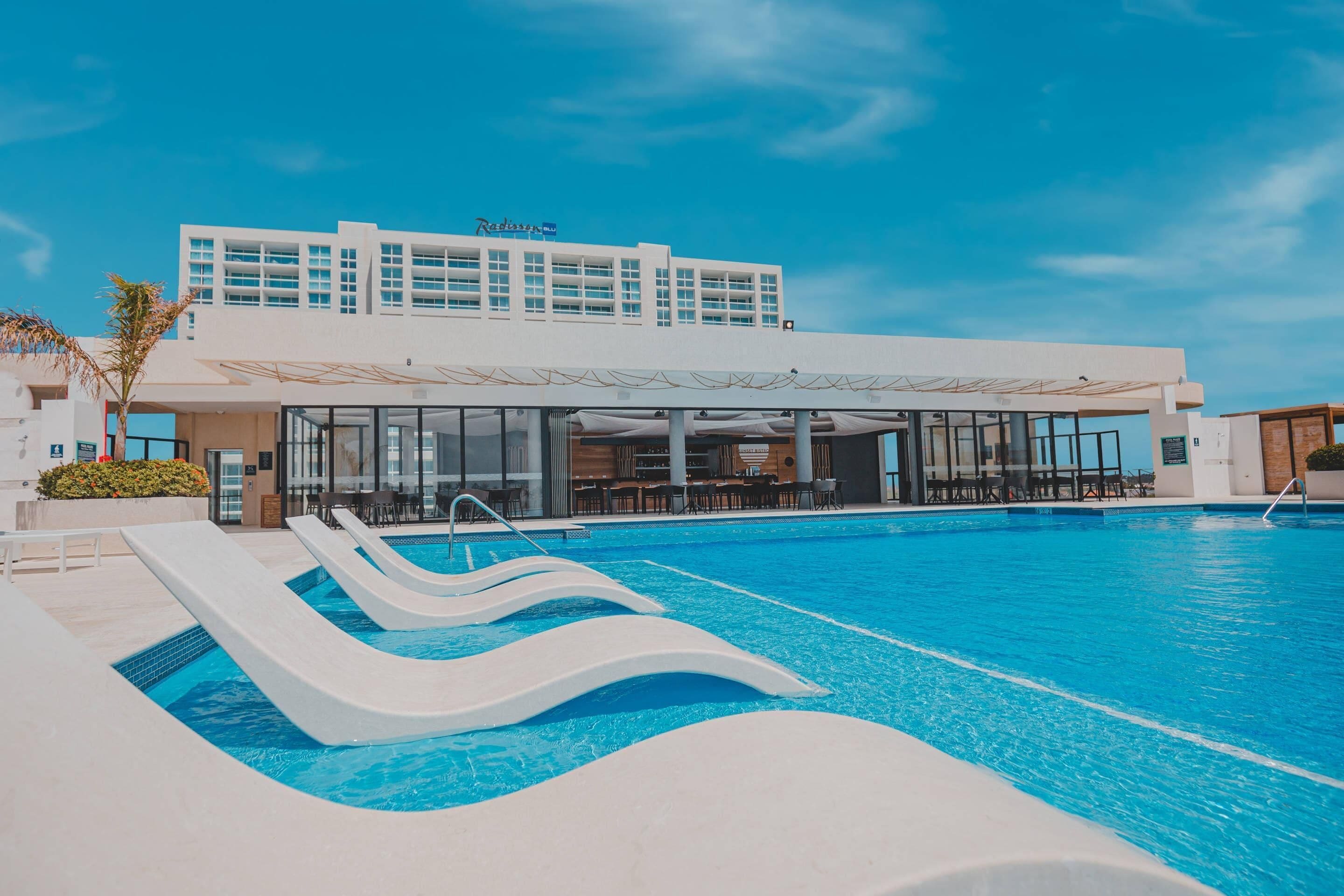 A hotel with a swimming pool, outdoor seating, and a modern building design.