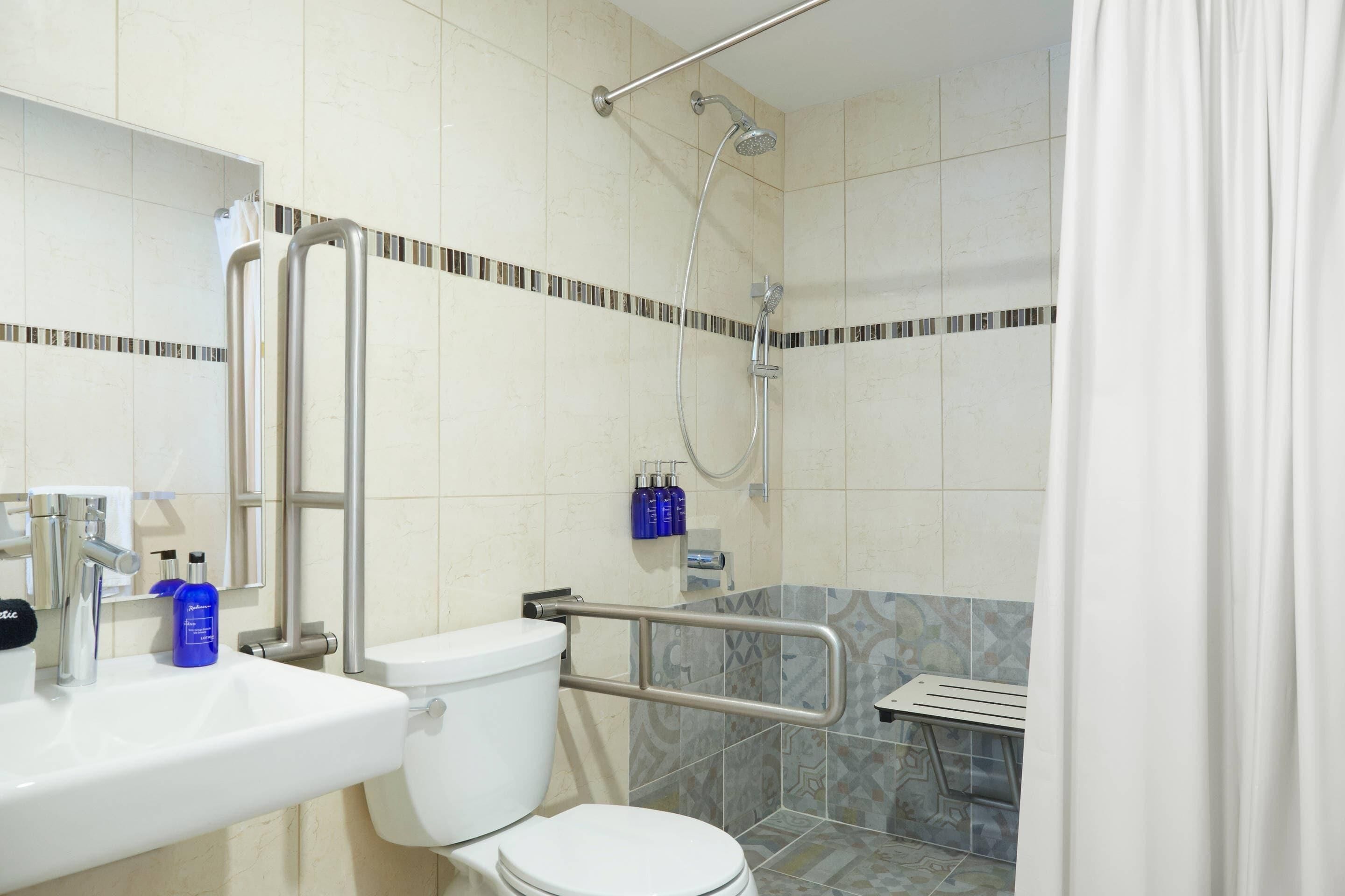 A bathroom with a white toilet, a sink, a shower with a handheld showerhead, and a grab bar.