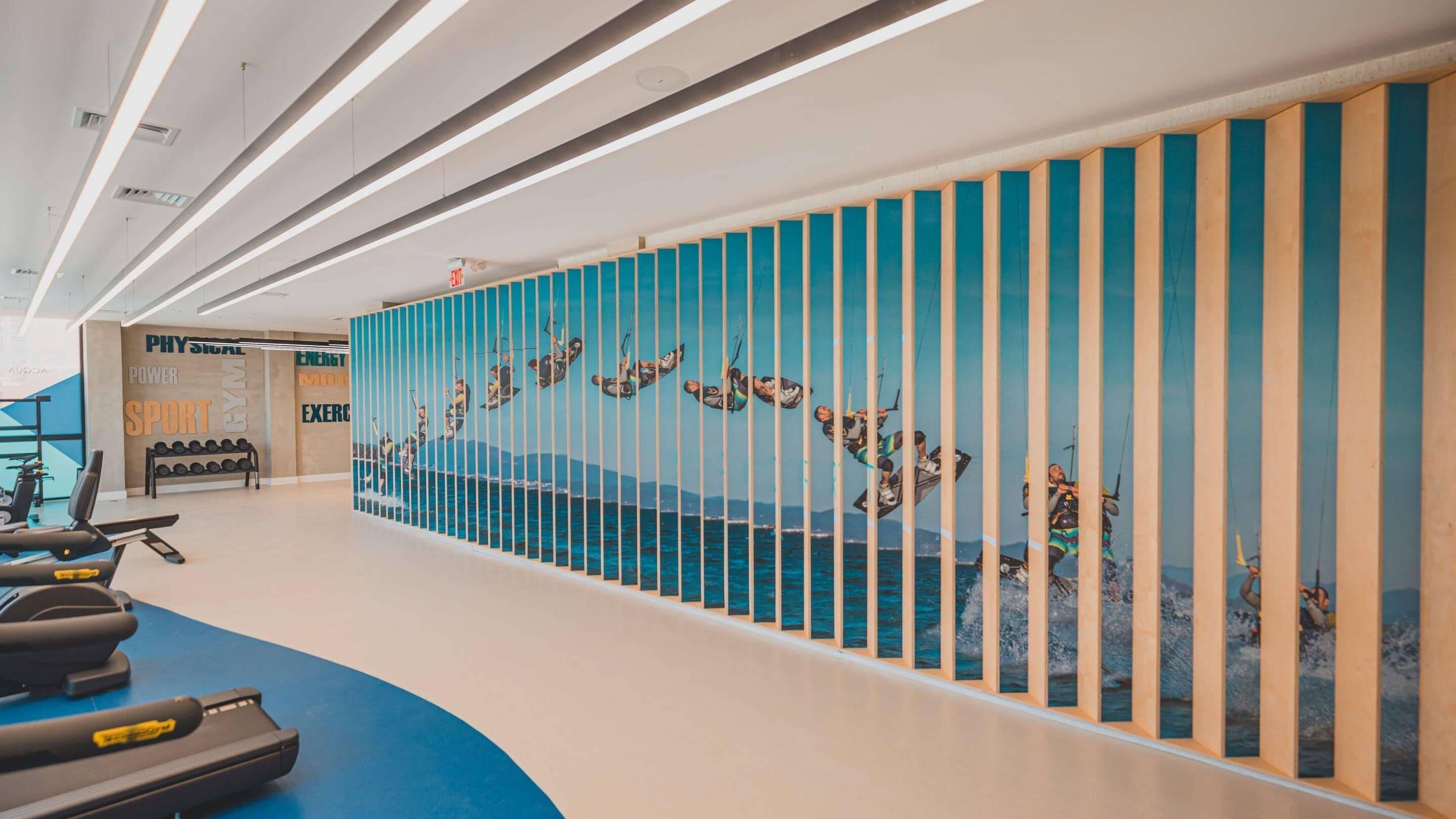 A gym with exercise equipment and a wall with vertical panels displaying images of people windsurfing.