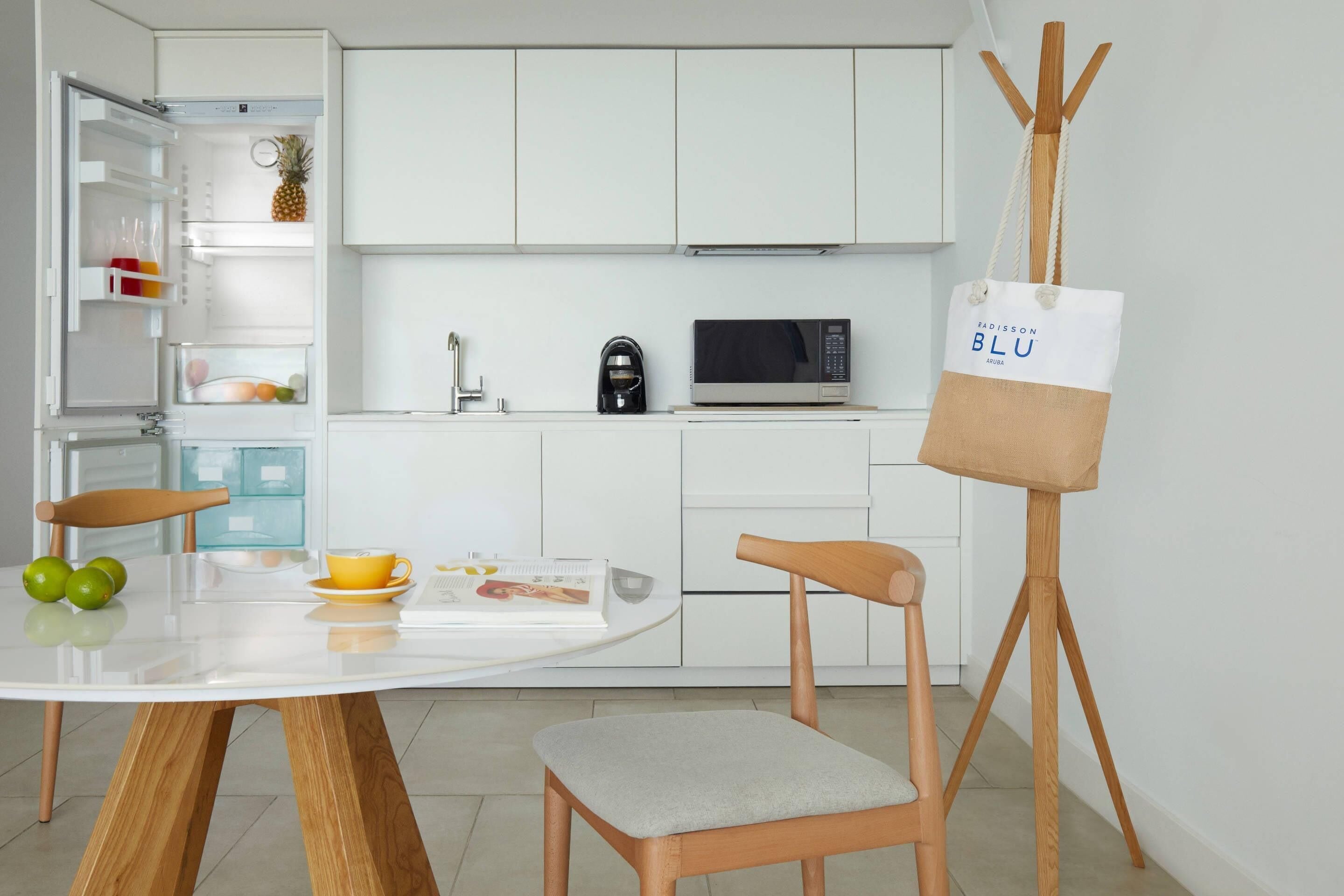 Una cocina moderna con armarios blancos, un microondas y una cafetera. Hay una mesa de comedor con sillas y una bolsa de alimentos en la encimera.
