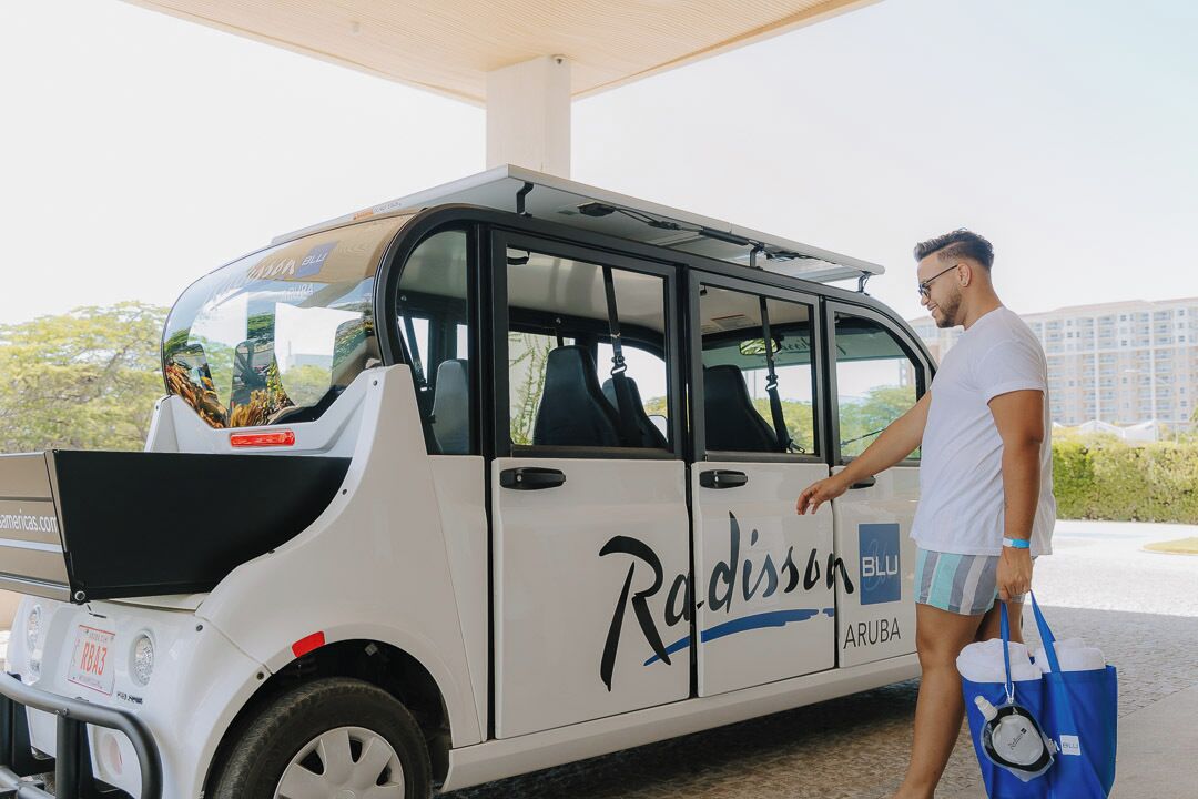 Un vehículo blanco Radisson Blu Aruba con puerta lateral y portaequipajes.