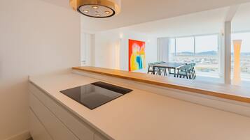A modern kitchen with a built-in tablet, a dining area with a table and chairs, and a large window offering a view of the city.