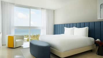 Ein modernes Hotelzimmer mit einem großen Bett, Meerblick, einem weißen Sessel und einem blauen Hocker.