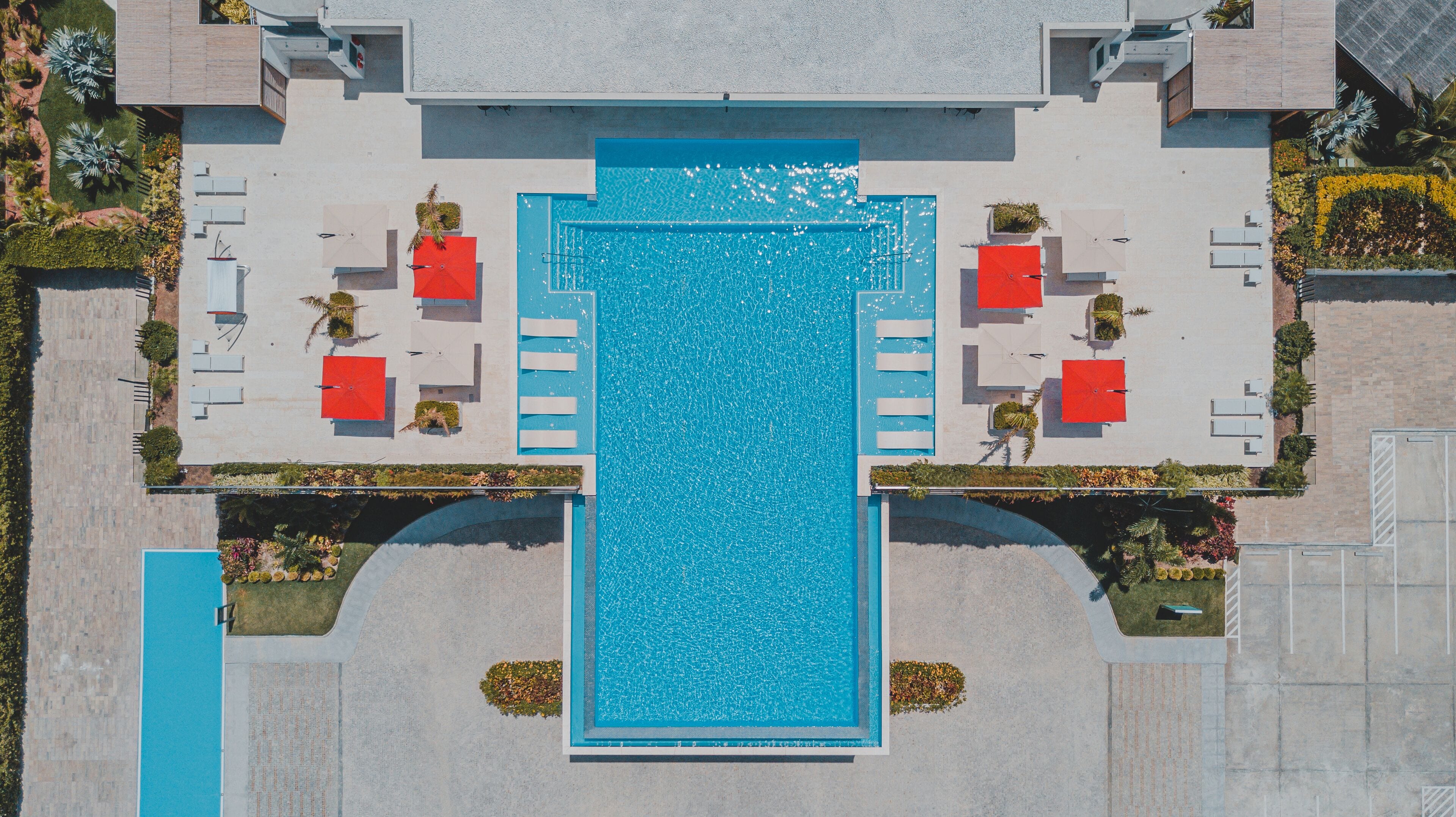 An aerial view of a hotel with a central swimming pool, multiple lounge areas, and a landscaped garden.