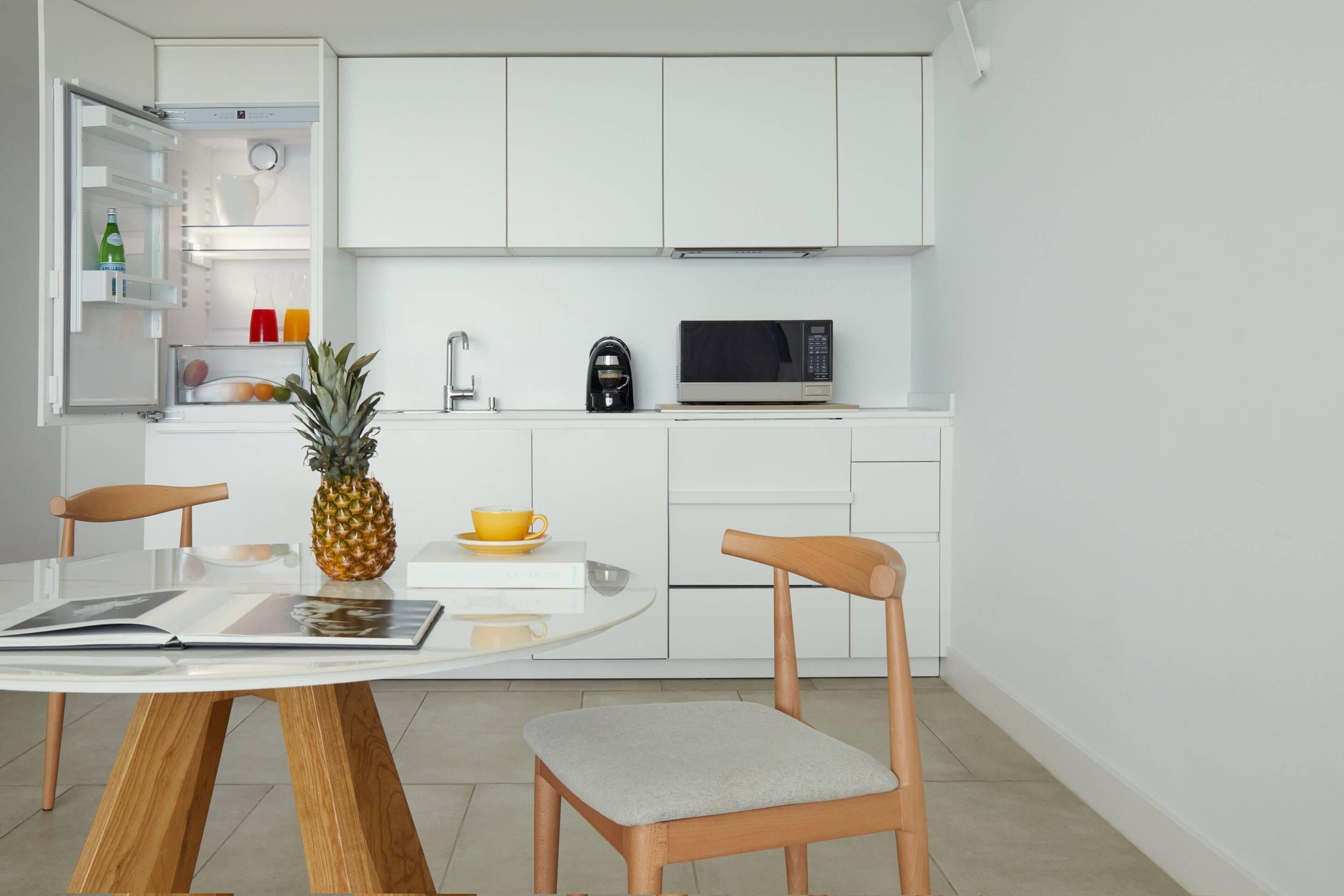 A modern kitchen with white cabinets, a microwave, a coffee maker, and a dining table with chairs.