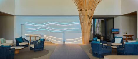 A modern lobby with blue wicker furniture, a central light installation, and a wooden ceiling structure.