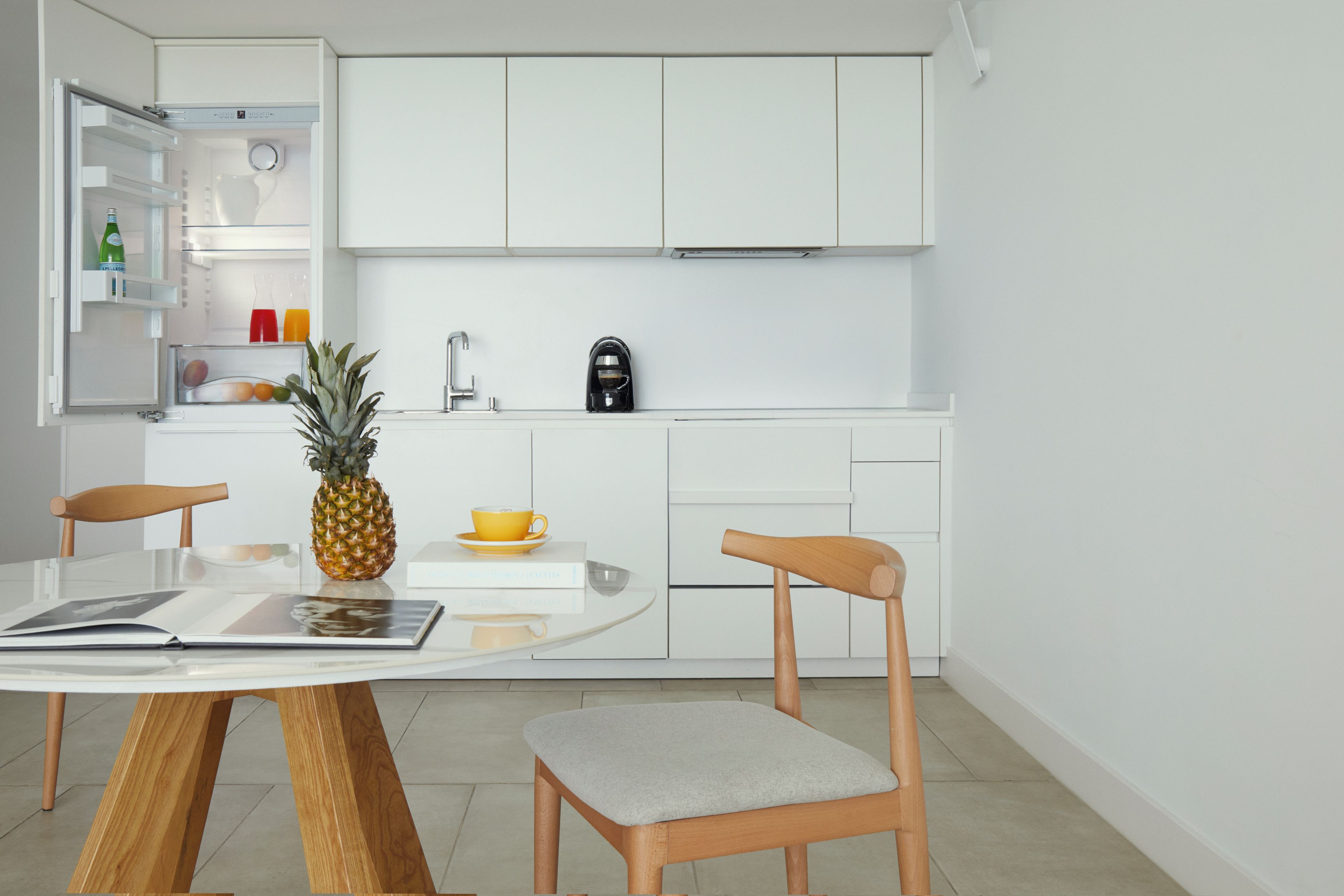 Een moderne keuken met witte kasten, een koffiezetapparaat en een eettafel met stoelen.