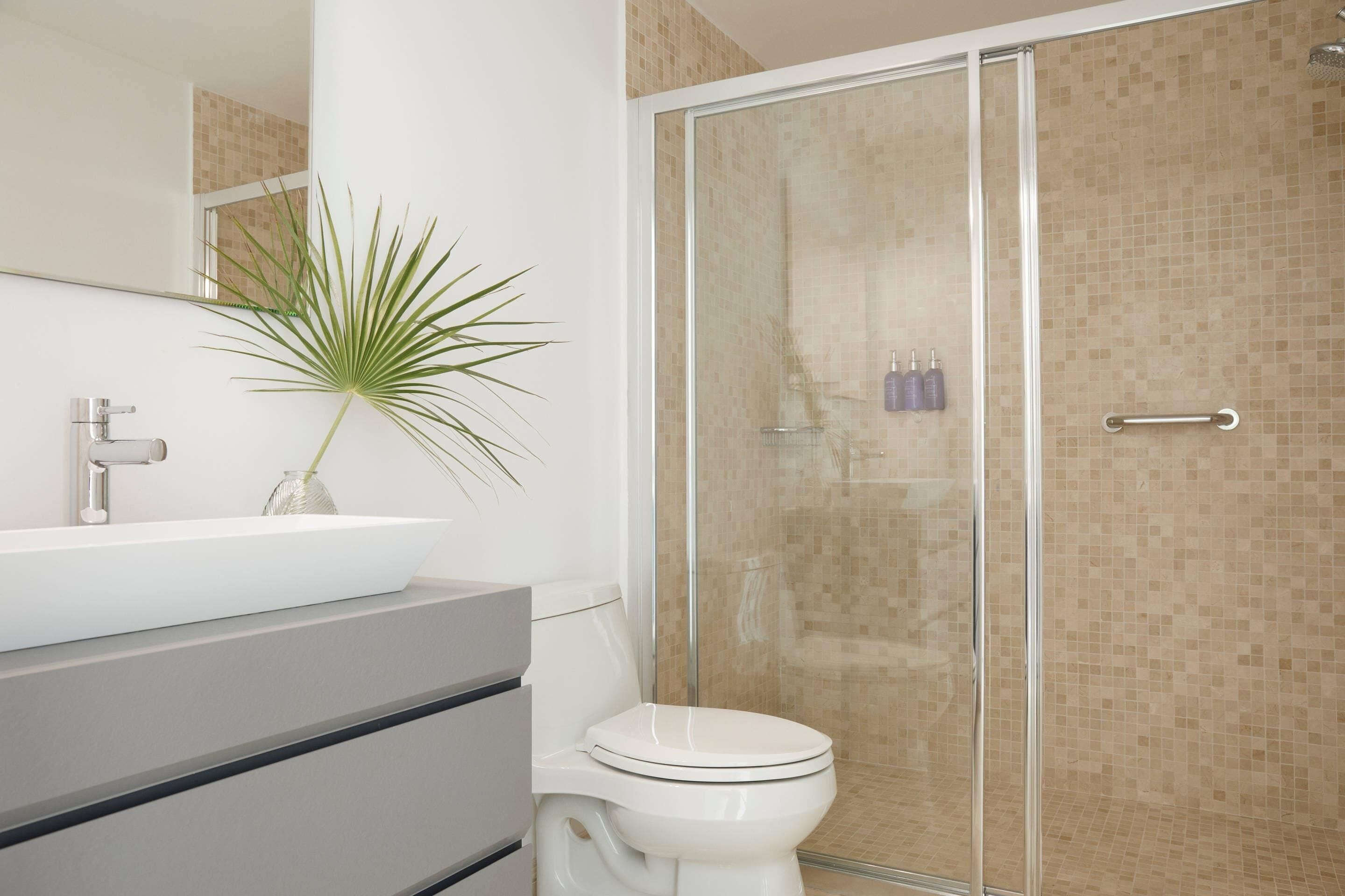 Un baño moderno con cabina de ducha de vidrio, un lavamanos blanco y un inodoro.
