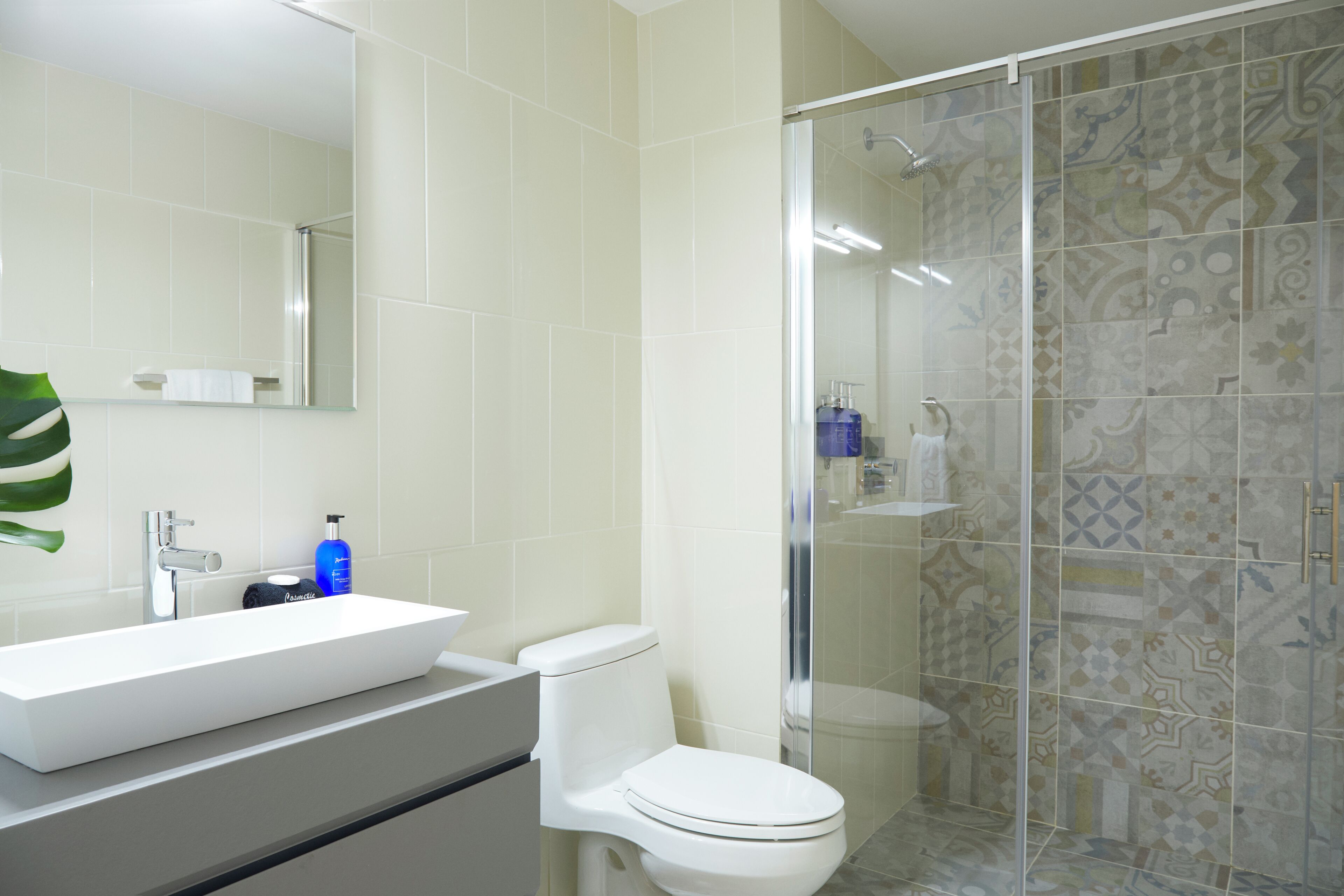 A bathroom with a white sink, a toilet, and a shower with patterned tiles.