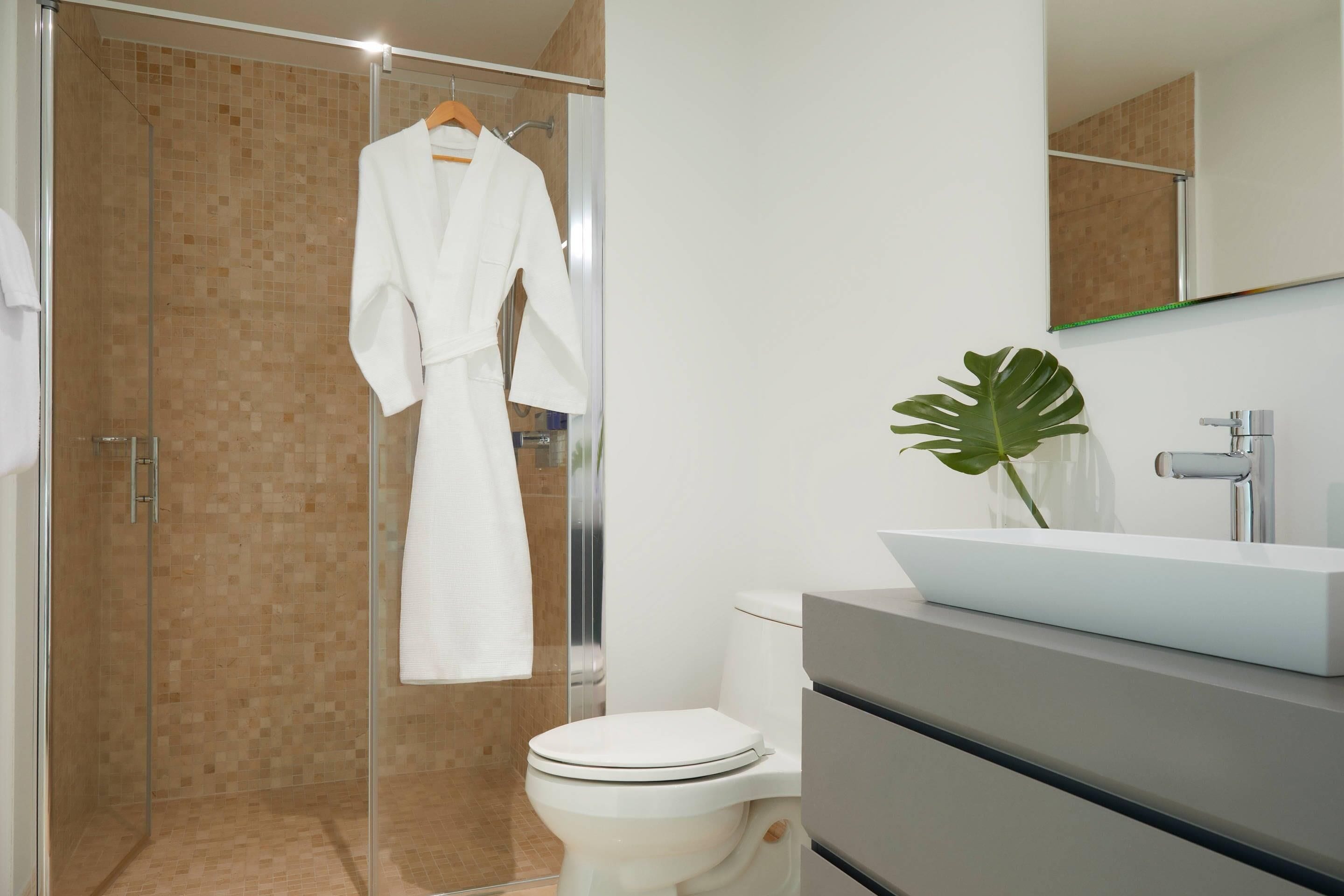 A modern bathroom with a glass-enclosed shower, a white toilet, a large mirror, and a white sink with a plant.
