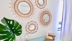 A room with a large green plant, a small bird decoration, and three woven wall art pieces. There are two remote controls on a light blue table. - Caíque – Charming 3-Bed Apartment in Olhão Downtown, Close to Ria Formosa (Olhão)