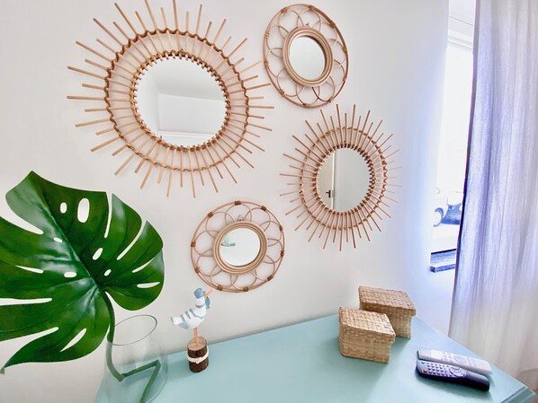 A room with a large green plant, a small bird decoration, and three woven wall art pieces. There are two remote controls on a light blue table.