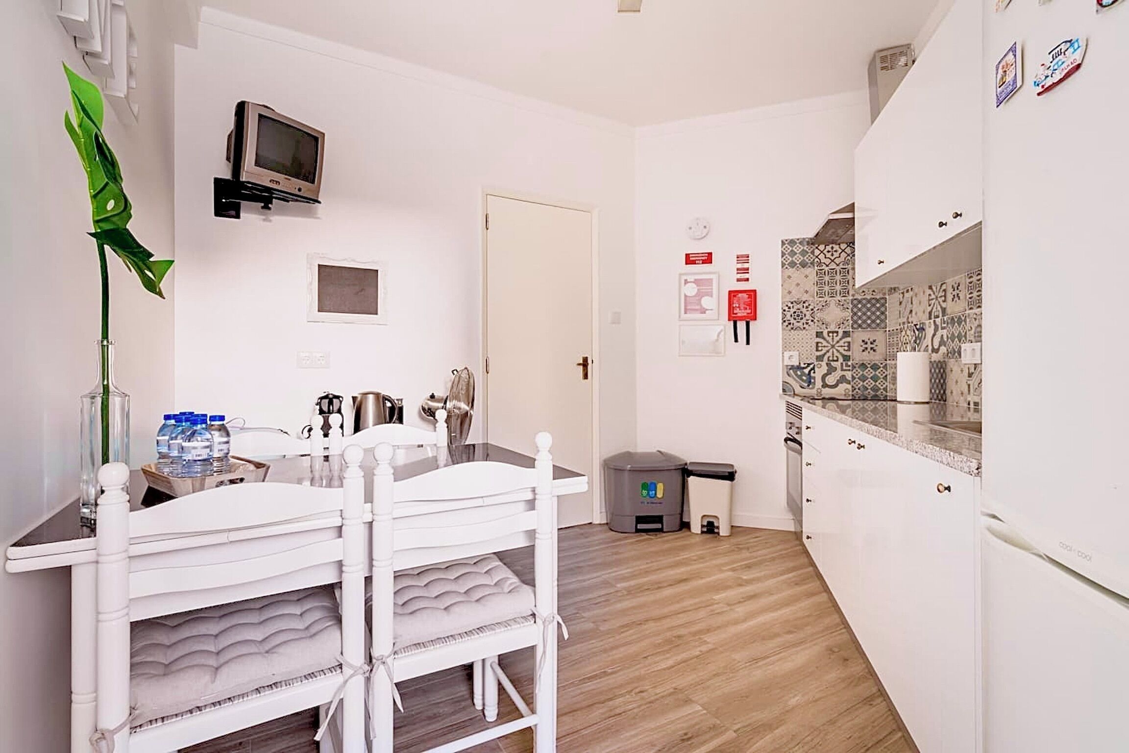 A compact kitchen with a white countertop, a sink, and a microwave. There is a trash bin and a door leading to another room.