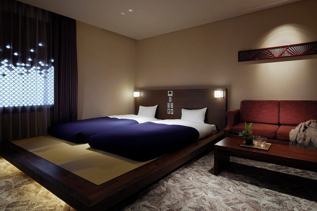 Een hotelkamer met een bed, een slaapbank, een klein tafeltje en een decoratief wandobject.