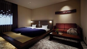 A hotel room with a bed, a sofa, a small table, and a decorative wall piece. - Minn Kanazawa (Kanazawa)