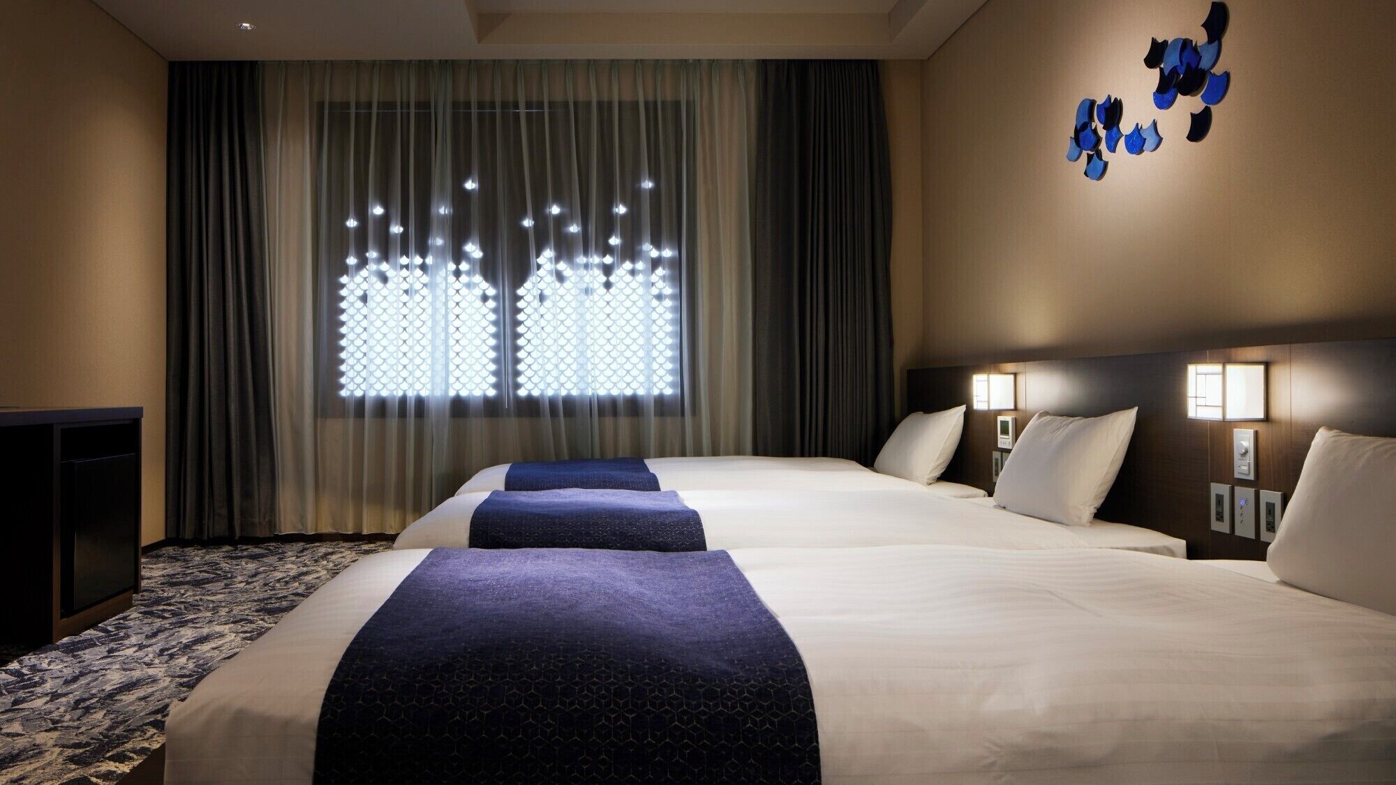 Habitación de hotel con una cama grande, dos mesitas de noche con lámparas, un escritorio y una ventana con cortinas.