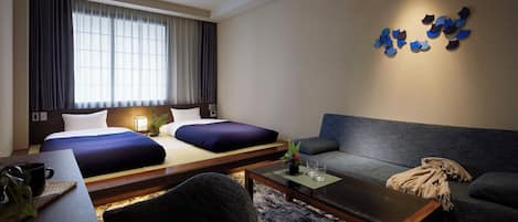 Una habitación de hotel con una cama, dos mesitas de noche, un sofá, una mesa de centro y una lámpara fijada a la pared.