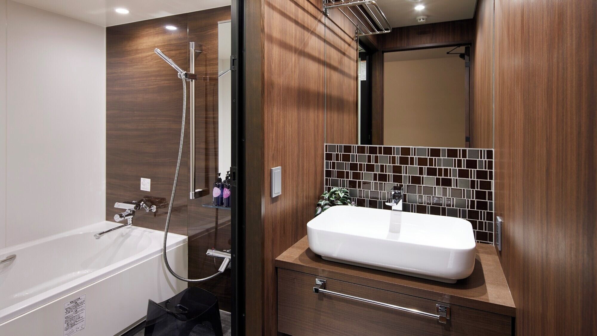 Un baño moderno con una bañera blanca, ducha con cerramiento de vidrio, lavamanos blanco y un salpicadero de azulejos negros, además de paneles de madera.