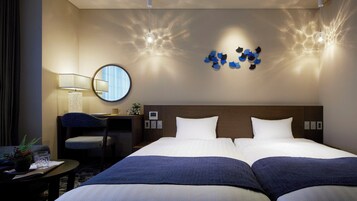 Habitación de hotel con dos camas, un escritorio con silla, un espejo redondo e iluminación en la pared.