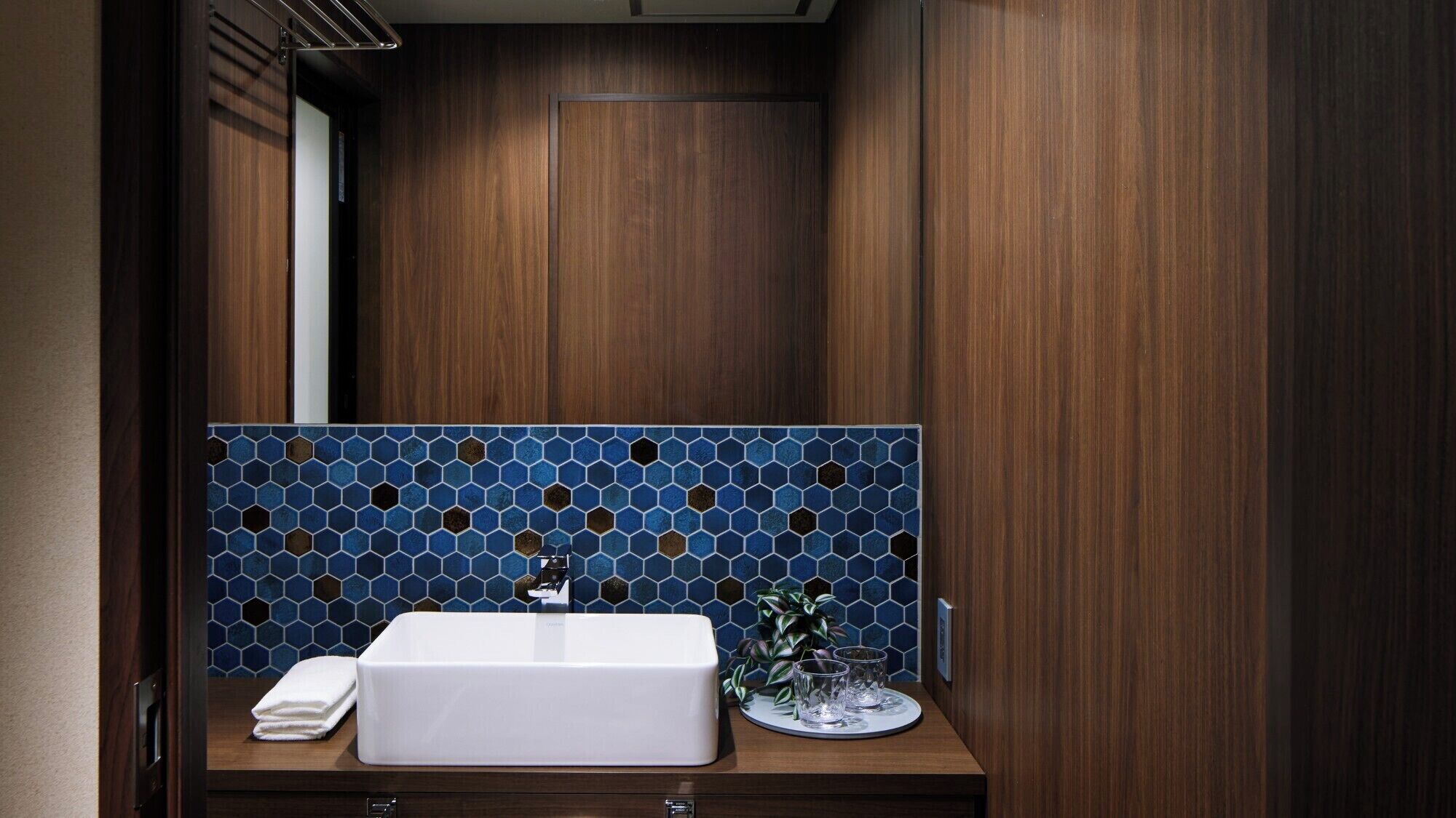 A bathroom with a wooden vanity, a white sink, and a blue hexagonal tile backsplash.