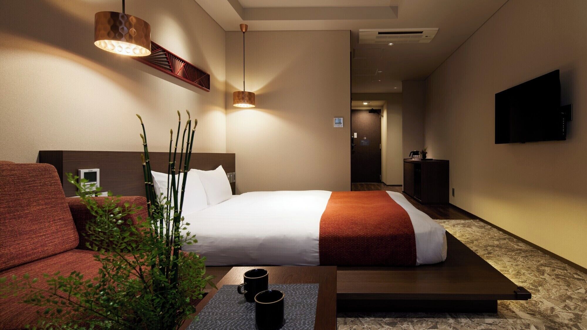A hotel room with a bed, a sofa, a coffee table, and a TV.